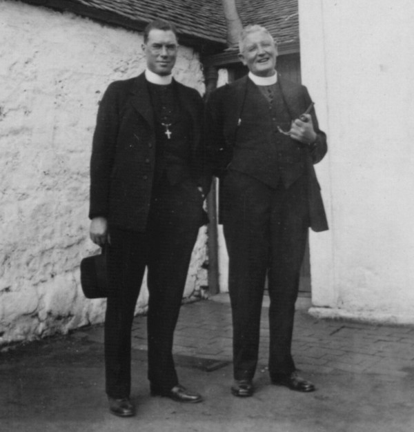 two priests standing by a farm building