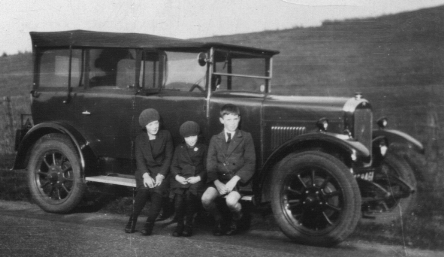 three children sitting on running board of old car
