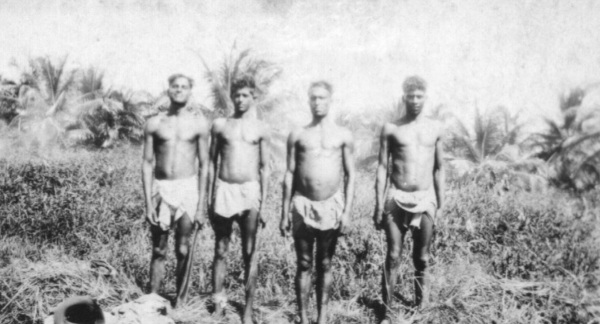 four bare-chested african men standing in grassland