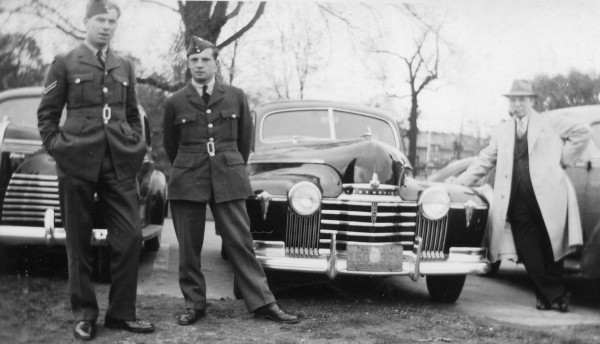 Two airmen in uniform with a civilan man leaning on an Oldsmobile car