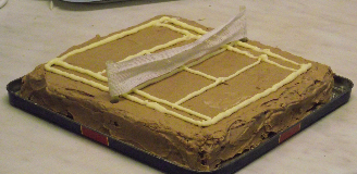 brown iced cake decorated as a clay tennis court